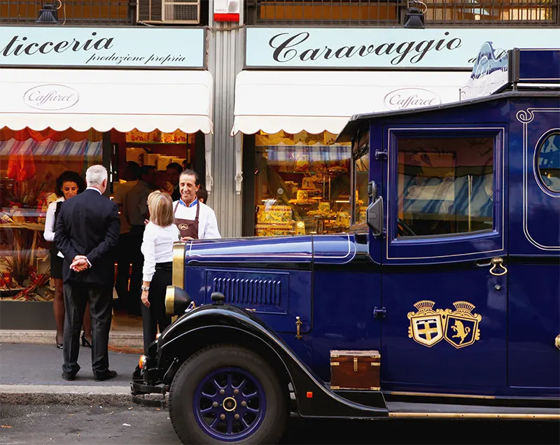 Un furgone d’epoca blu con la scritta Caravaggio davanti alla vetrina della pasticceria