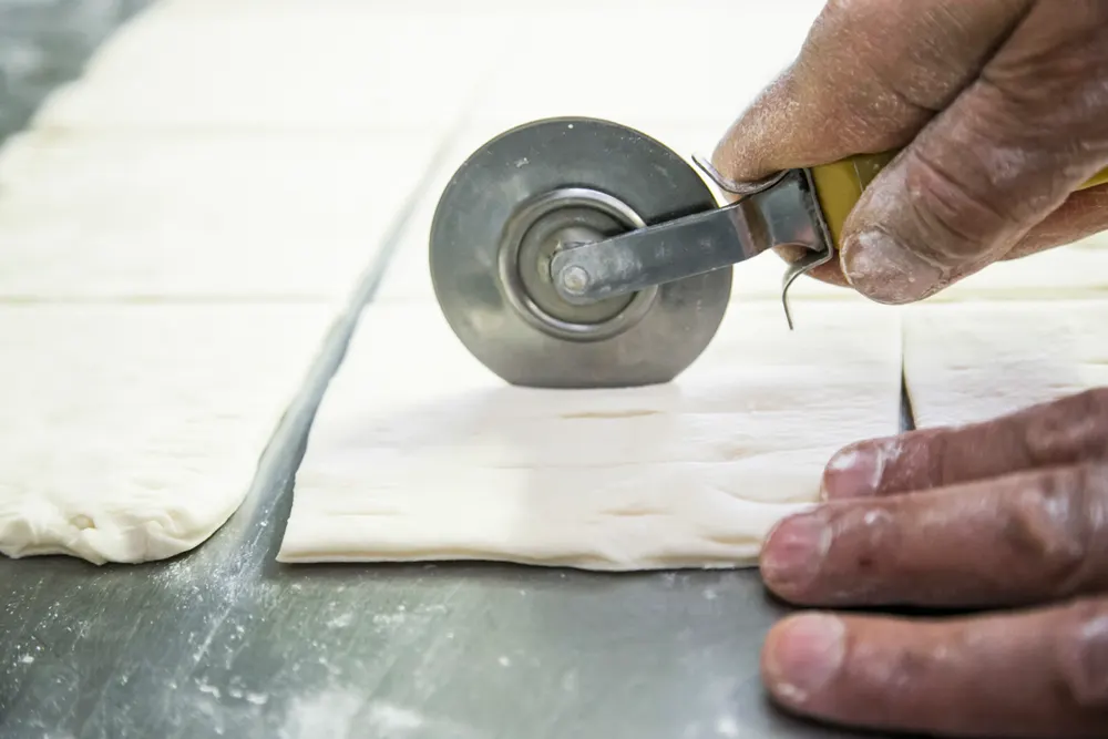 Le mani del pasticcere che tagliano la pasta sfoglia con una rotella